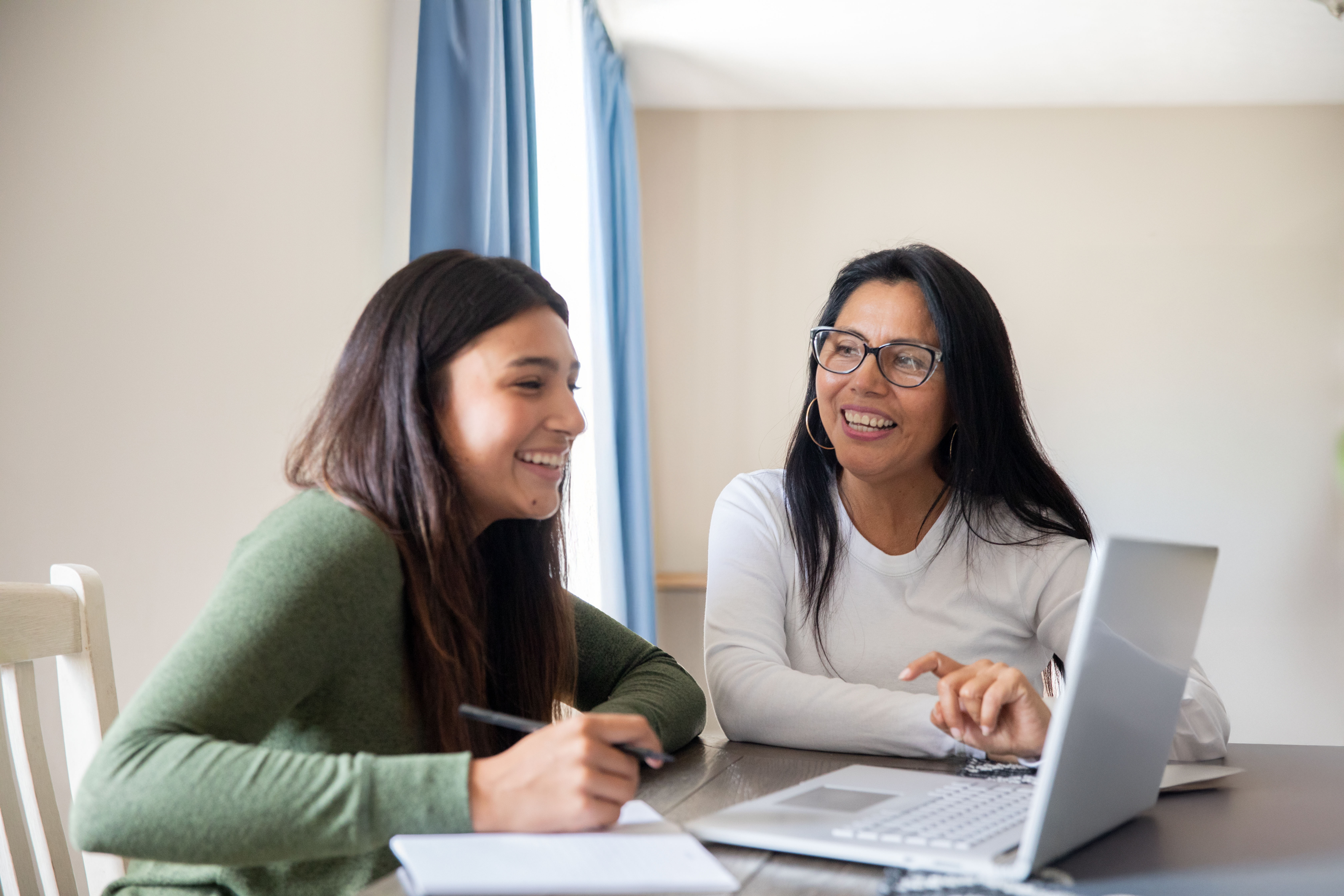 Two smiling young women at a desk looking at a computer.