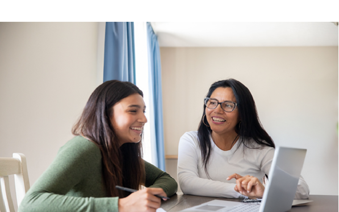 Two smiling women sitting at a desk looking at a computer.